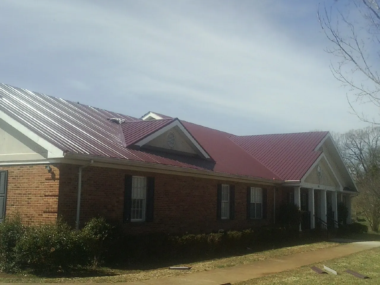Red metal roof with gabled entries on a long brick building, from a Hail Damage Roof Repair job in Hayfield