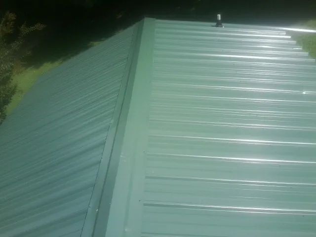 New green metal panels meeting at the ridge of a roof — Flat Roof Repair work by our crew in Hayfield
