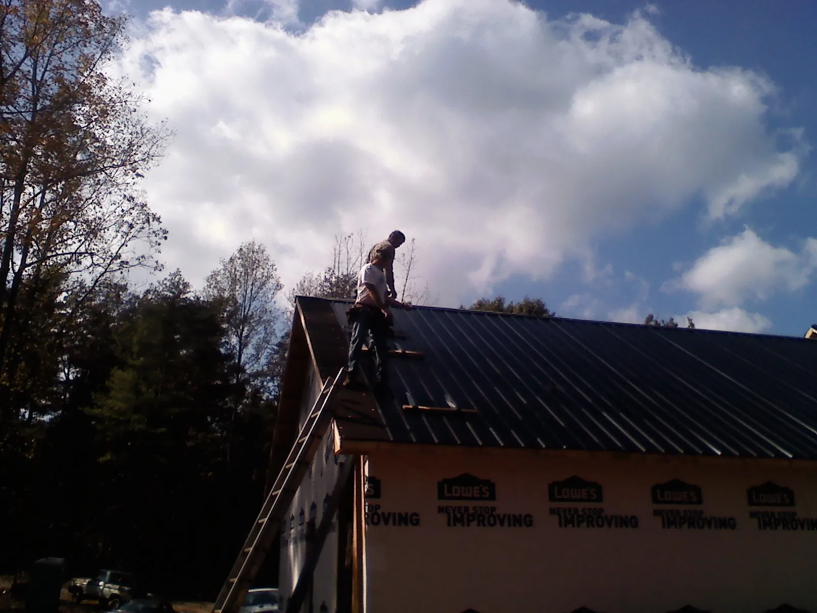 Roofer fastening dark metal panels high against a cloudy sky, from a Roof Inspection job in Hayfield