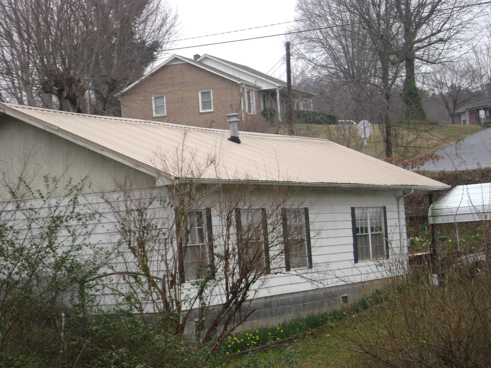 Tan metal roof on a white sided house set into a hillside — Commercial Roofing by Roofing Brothers in Hayfield