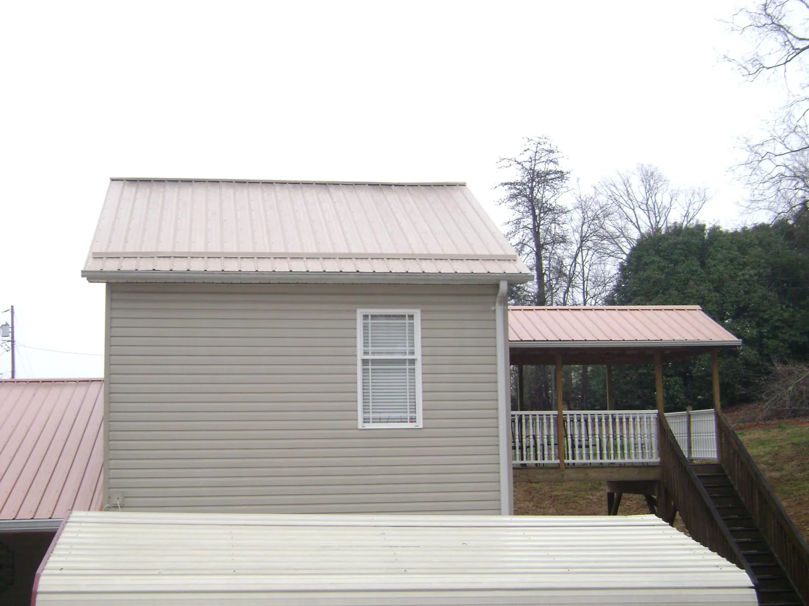 Tan metal roofs on a two story addition and attached porch, from a Roof Replacement job in Hayfield